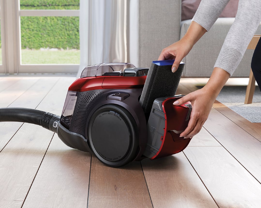 Hands removing the filter from a red Electrolux vacuum cleaner on a wooden floor