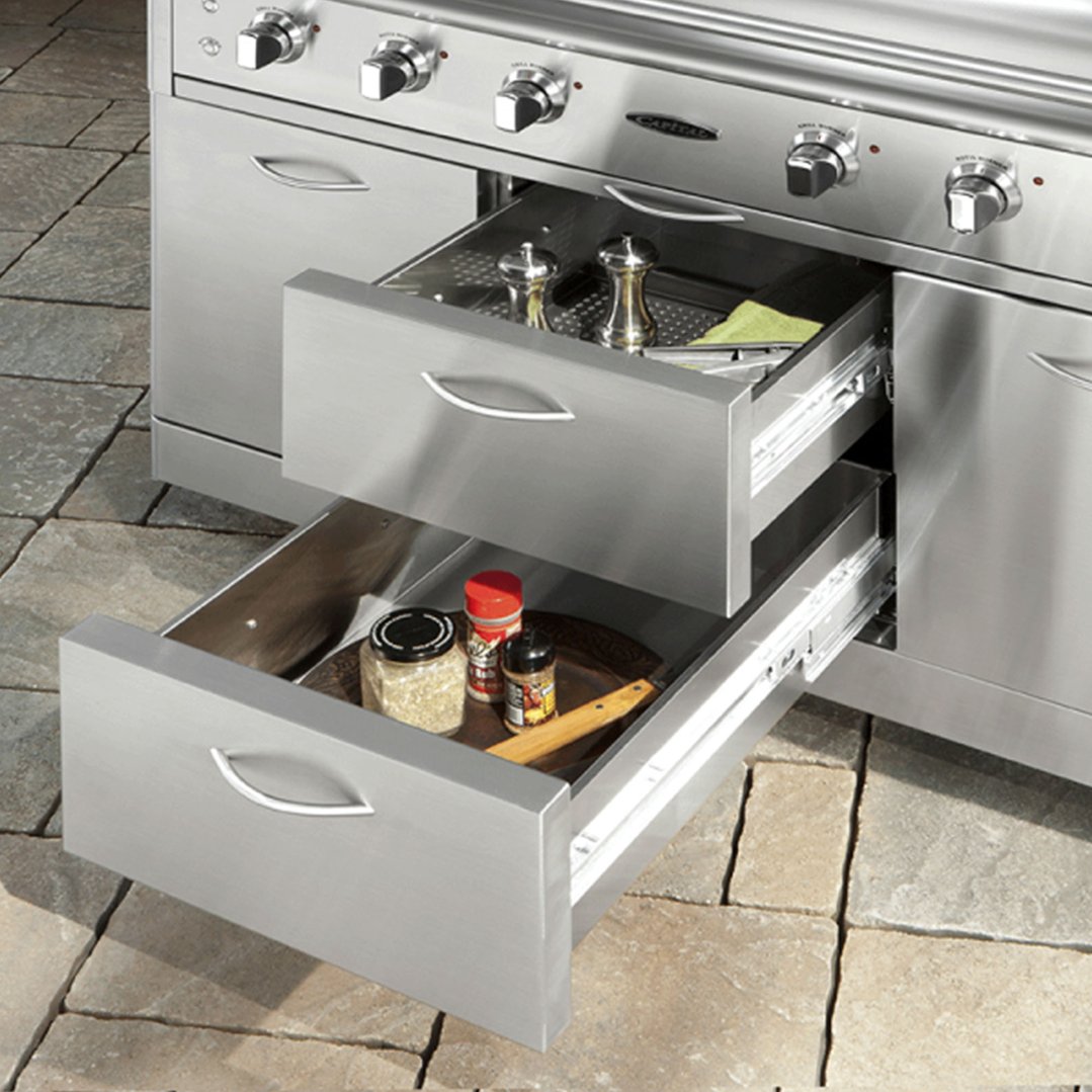 Stainless steel outdoor barbecue with two open drawers containing spices and shakers