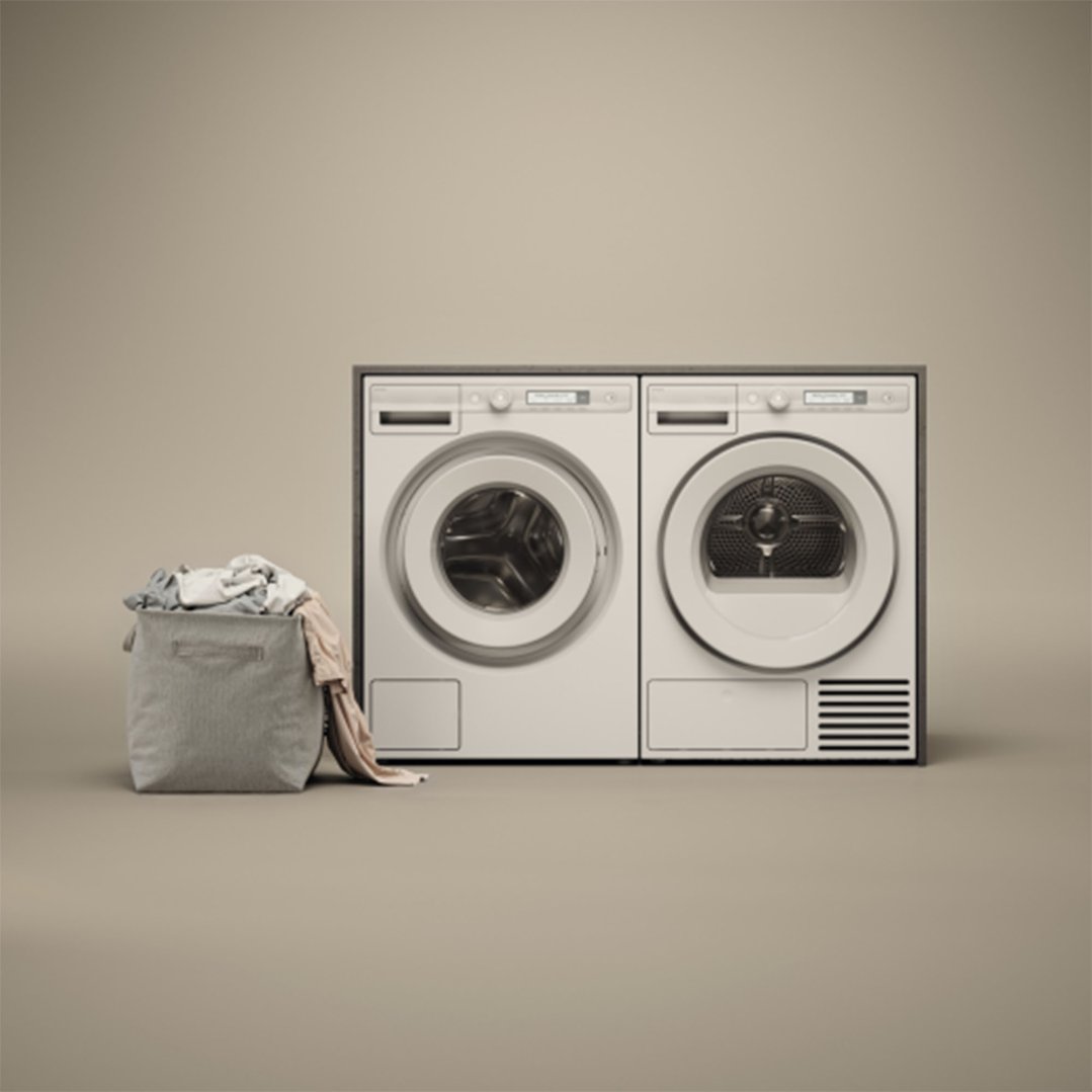 Two dryers and a laundry basket with clothes on a neutral background