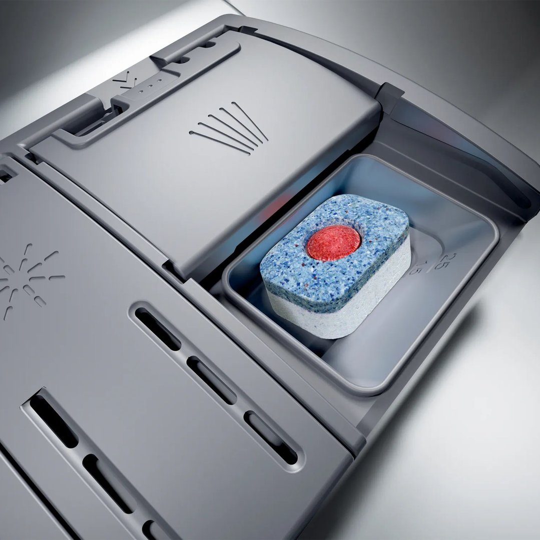 A dishwasher detergent tablet in the dispenser of a dishwasher