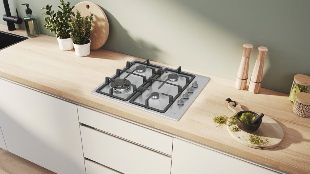 Gas cooktop built into a light wood kitchen counter with plants and spices