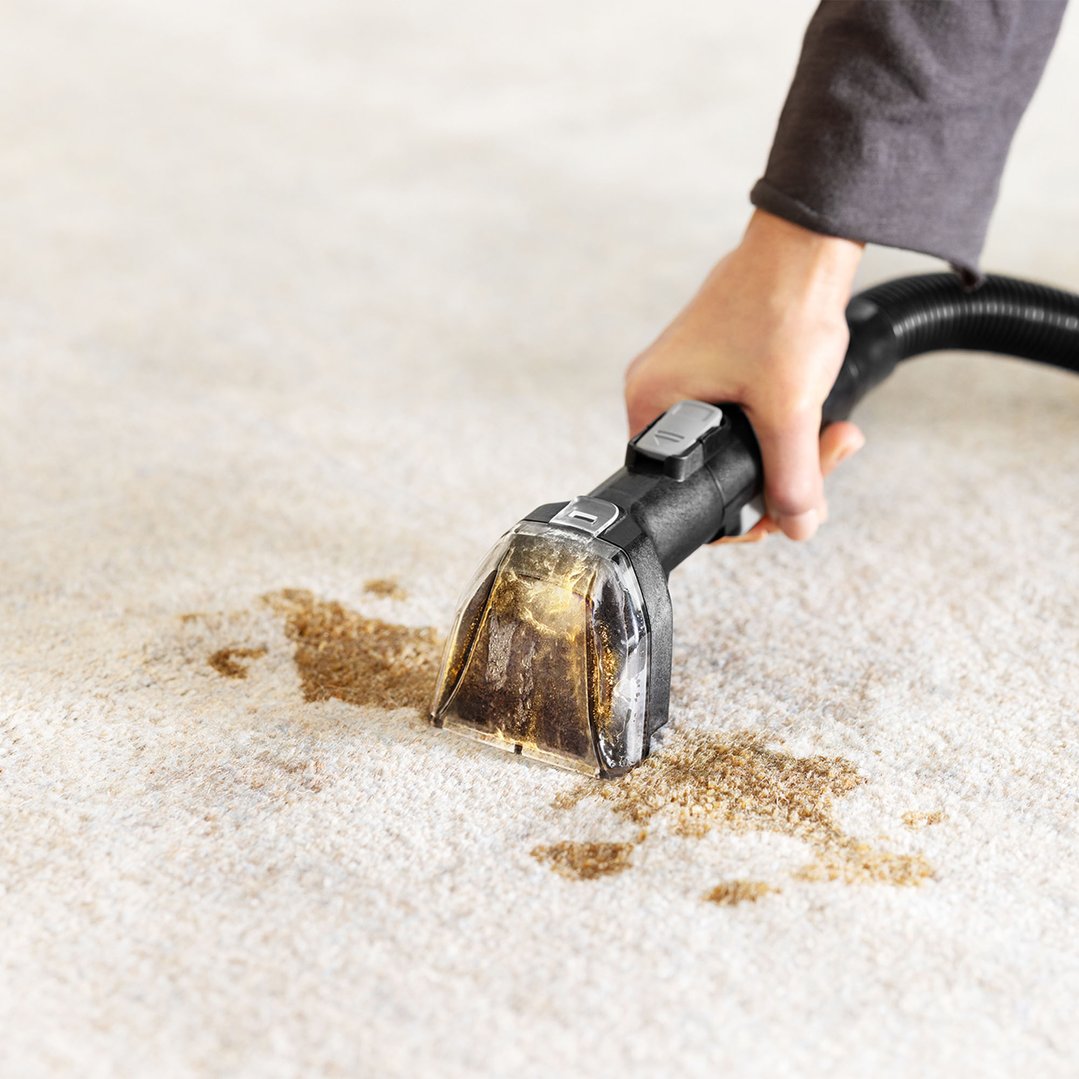 Hand using a BISSELL SpotClean HydroSteam to clean a stain on carpet