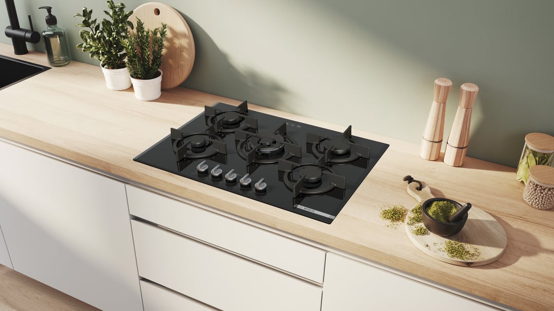 Black gas cooktop with five burners on a light wood kitchen counter