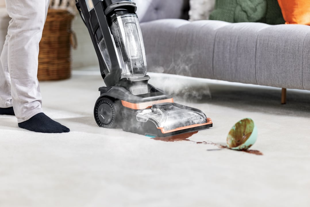 Person cleaning a spilled drink on a carpet with a BISSELL Revolution HydroSteam vacuum cleaner