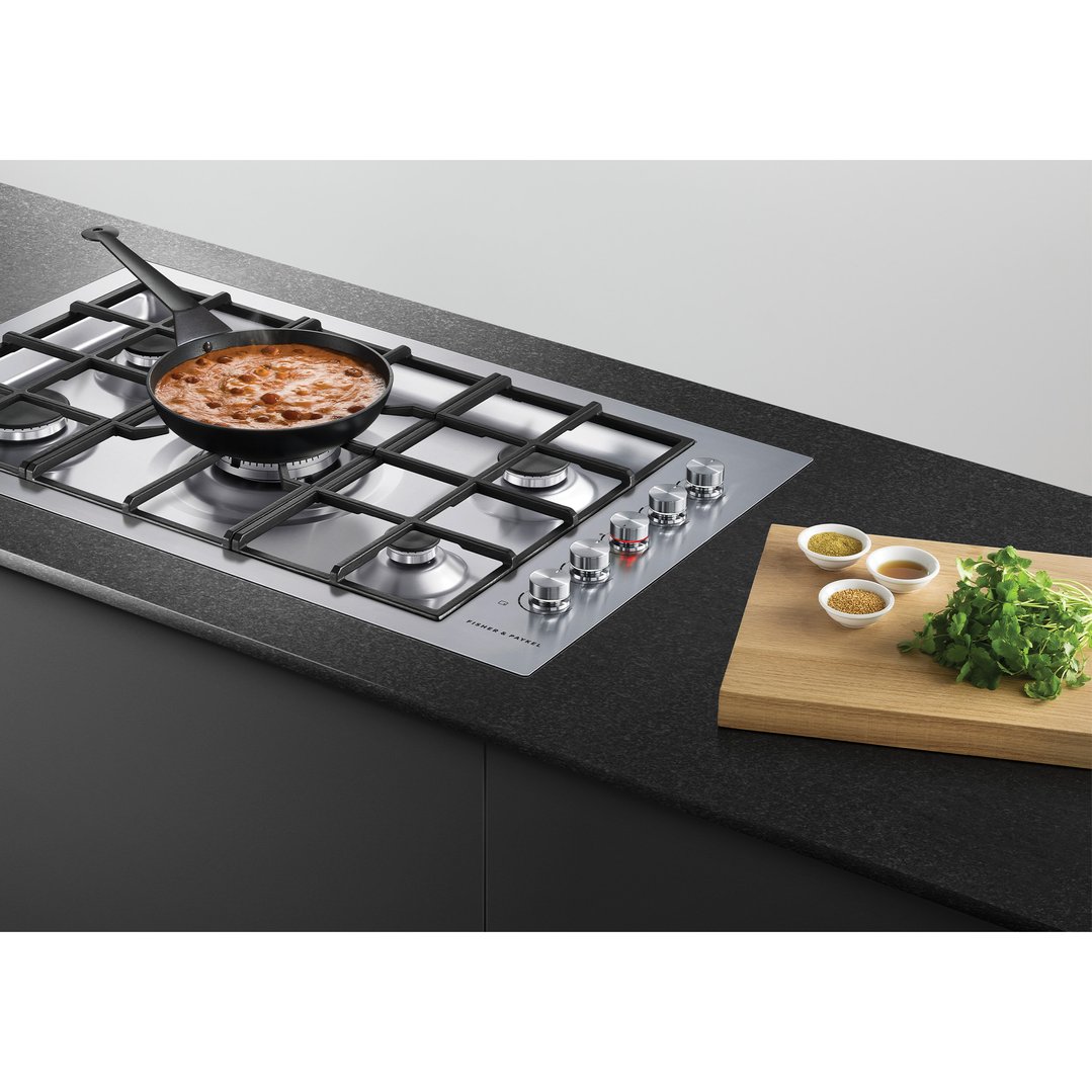 A gas cooktop with a pan of food and spices on a wooden board