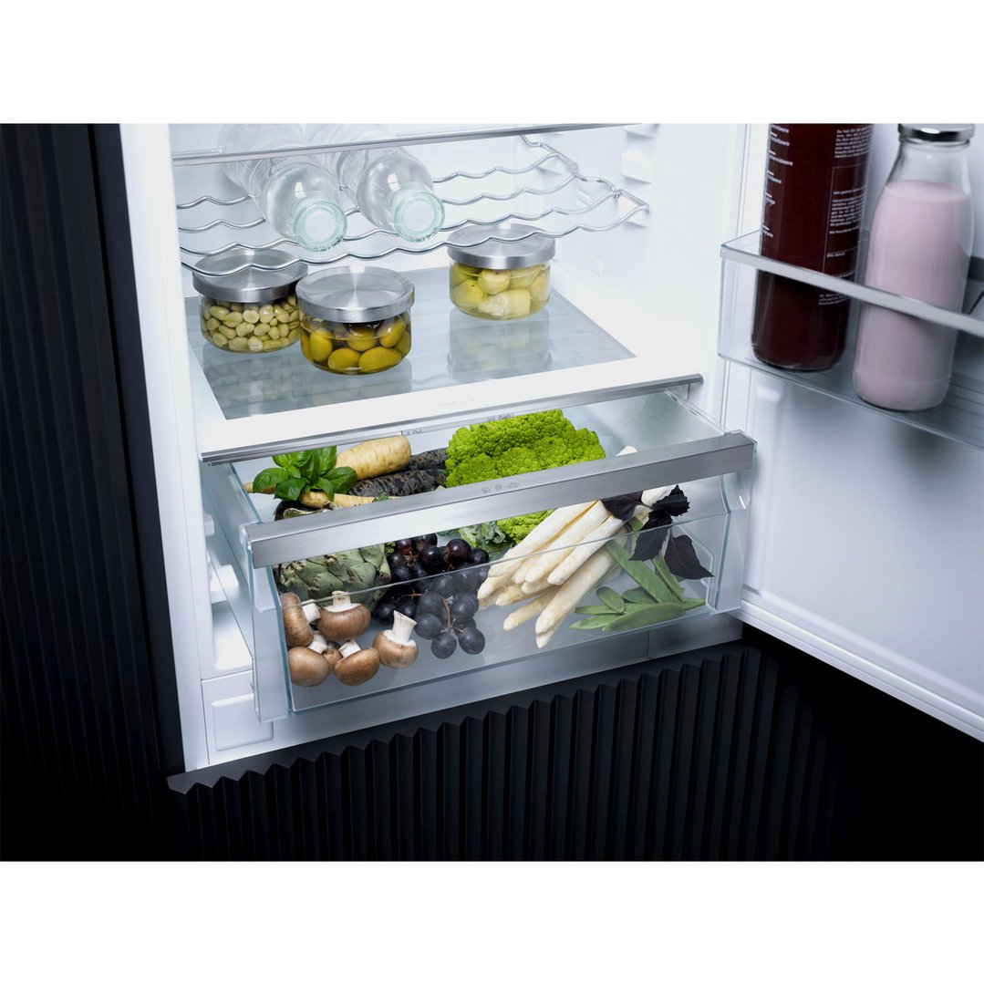 Open integrated bottom mount fridge with food items on shelves and in drawers