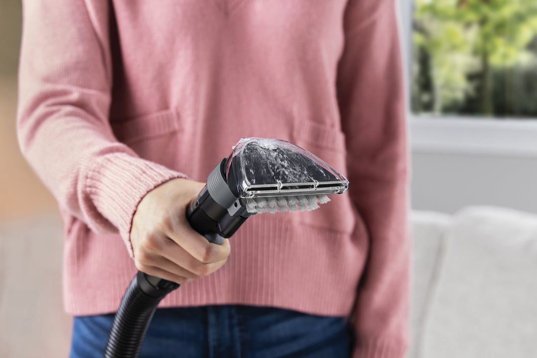 Person holding a carpet and upholstery cleaner with a brush head and foamy water