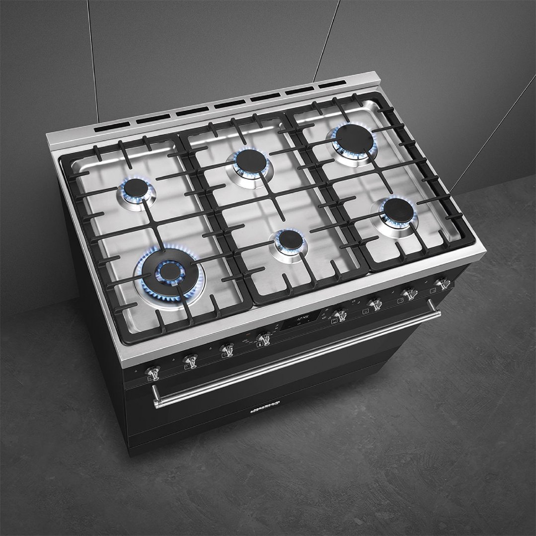 Black freestanding cooker with six gas burners on a dark grey floor