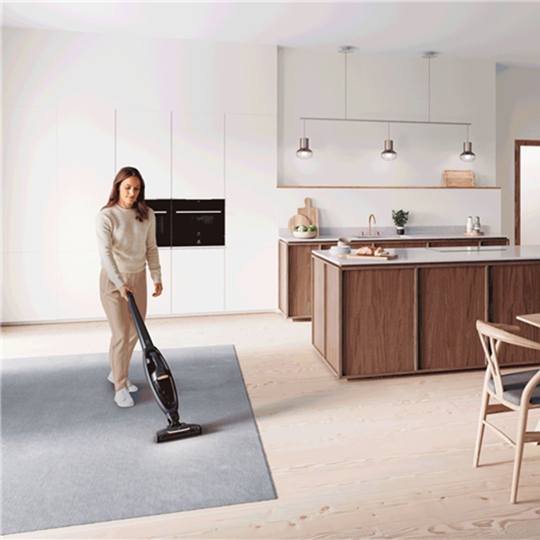 Woman vacuuming a grey rug in a modern kitchen with a cordless vacuum