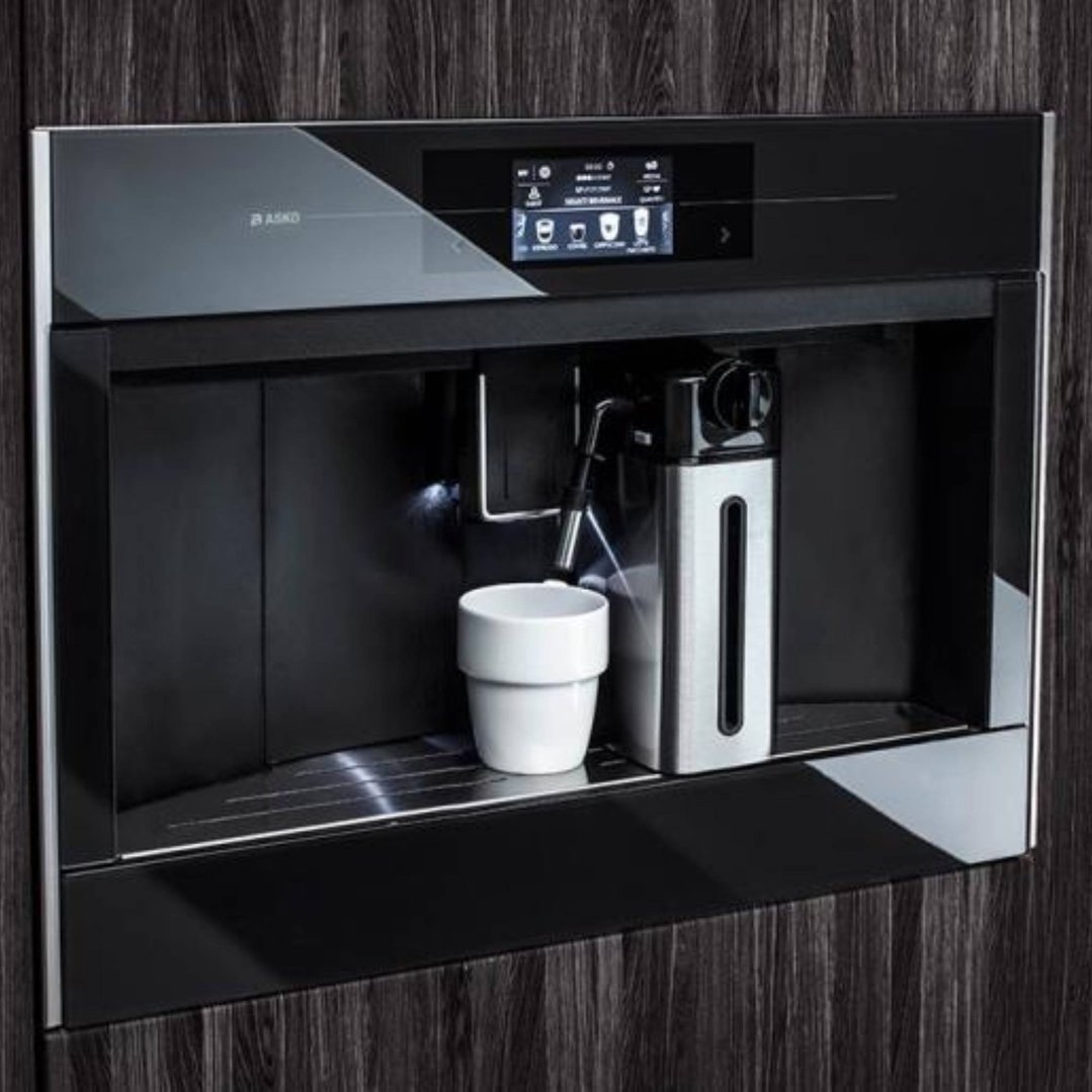 Built-in coffee machine with a white cup on the drip tray in a dark wood kitchen