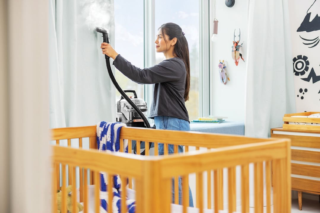 Woman steam cleaning curtains with a BISSELL SpotClean HydroSteam in a nursery