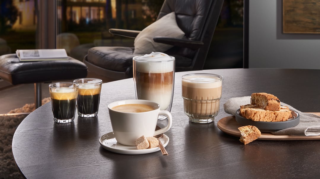 Various coffee drinks and biscotti on a dark wooden table in a living room