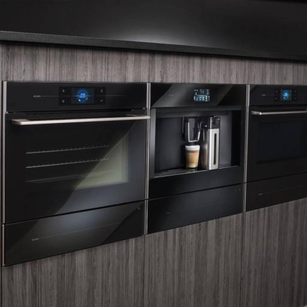 Built-in coffee machine and two ovens in a dark wood kitchen